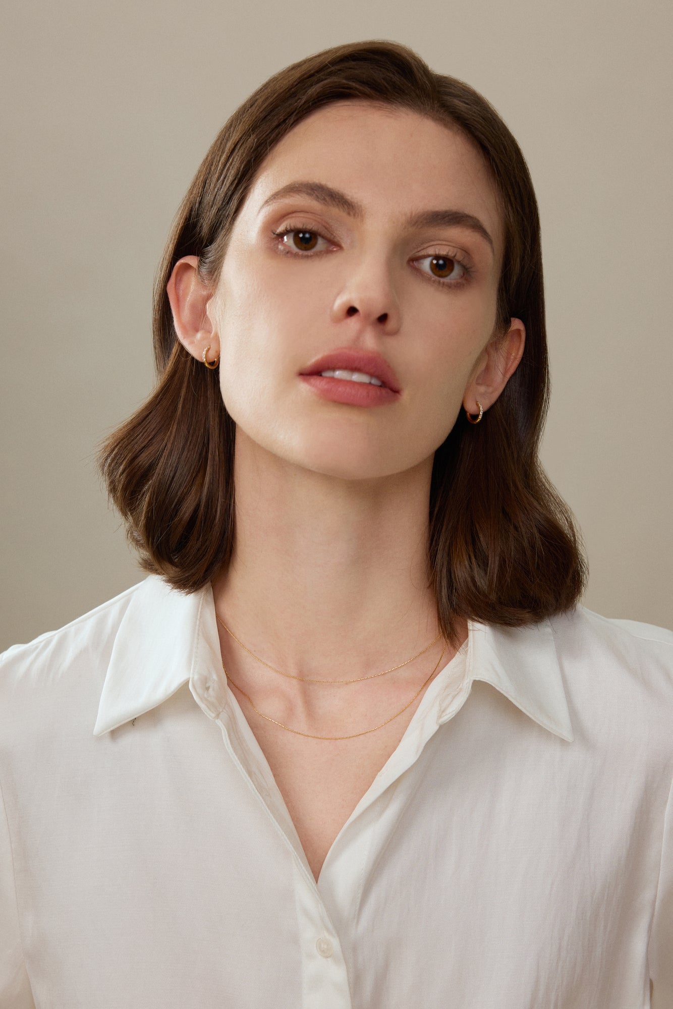 Model trägt filigrane Huggie Creolen aus 18K Gold mit Labordiamanten zu feinen Goldketten.