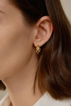 Nahaufnahme einer skulpturalen Triple Creole aus massivem 18K Gold am Ohr getragen.