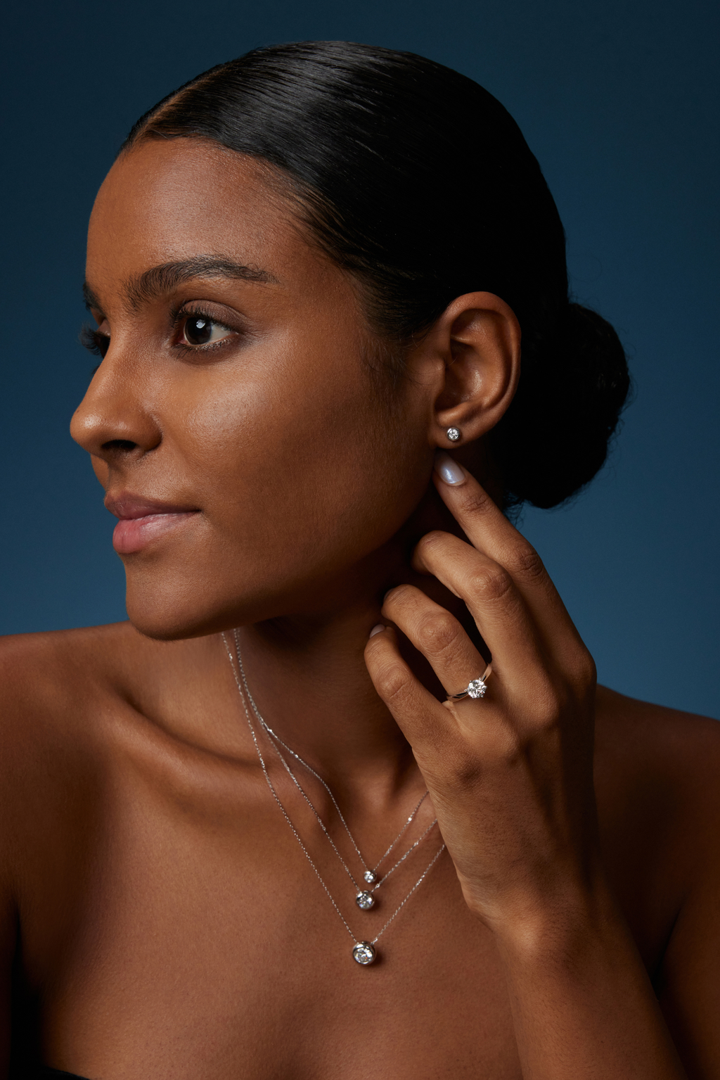 Model trägt drei Solitär-Diamantketten aus 18K Weißgold mit runden Labordiamanten in unterschiedlichen Größen sowie passende Diamant-Ohrstecker und einen Solitärring.