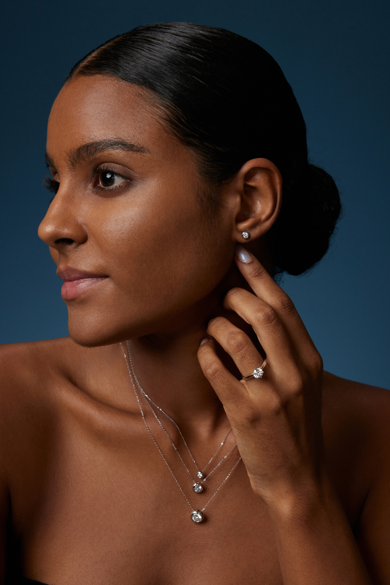 Model trägt drei Solitär-Diamantketten aus 18K Weißgold mit runden Labordiamanten in unterschiedlichen Größen sowie passende Diamant-Ohrstecker und einen Solitärring.